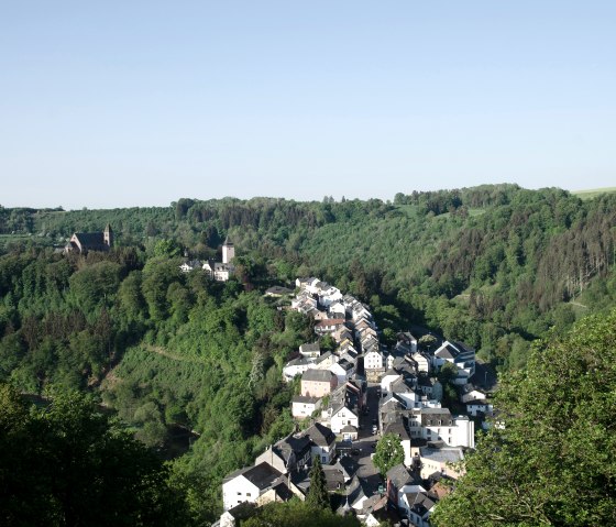 Panoramablick auf Kyllburg, umgeben von dichten Wäldern und Hügeln, mit einer Kirche und Häusern im Tal., © TI Bitburger Land Panoramablick auf Kyllburg, umgeben von dichten Wäldern und Hügeln, mit einer Kirche und Häusern im Tal., © TI Bitburger Land