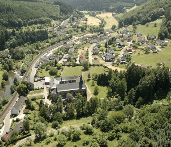 Vue aérienne d'un village avec une église au premier plan, entouré de forêts et de champs. Une ligne de chemin de fer traverse le village., © Rudolf Höser Vue aérienne d'un village avec une église au premier plan, entouré de forêts et de champs. Une ligne de chemin de fer traverse le village., © Rudolf Höser
