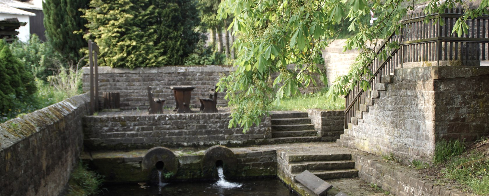 Ancien lavoir avec bassin, murs de pierre et escaliers, entouré de végétation verte et d'arbres., © Monika Bach Ancien lavoir avec bassin, murs de pierre et escaliers, entouré de végétation verte et d'arbres., © Monika Bach