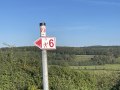 Een wegwijzer met de nummers 6 en 73 staat voor een groen, bebost landschap onder een blauwe hemel., © André Szybalsky Een wegwijzer met de nummers 6 en 73 staat voor een groen, bebost landschap onder een blauwe hemel., © André Szybalsky
