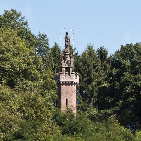 Die Mariensäule in Kyllburg ragt aus dichtem Wald hervor. Eine Statue steht auf einem steinernen Turm, umgeben von grünen Bäumen und blauem Himmel., © TI Bitburger Land Die Mariensäule in Kyllburg ragt aus dichtem Wald hervor. Eine Statue steht auf einem steinernen Turm, umgeben von grünen Bäumen und blauem Himmel., © TI Bitburger Land