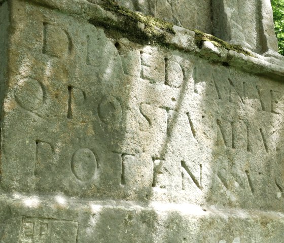 Close-up van een oude inscriptie op een verweerd stenen monument, omgeven door mos en bos., © Elke Wagner, Felsenland Südeifel Tourismus GmbH Close-up van een oude inscriptie op een verweerd stenen monument, omgeven door mos en bos., © Elke Wagner, Felsenland Südeifel Tourismus GmbH