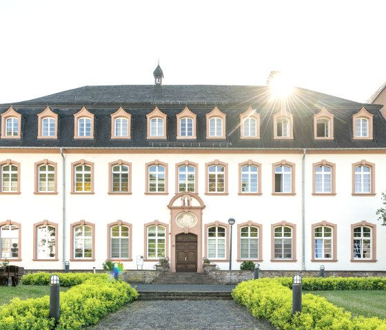 Un bâtiment historique avec une façade symétrique, de nombreuses fenêtres et un jardin bien entretenu. Le soleil brille derrière le toit., © Eifel Tourismus GmbH, Dominik Ketz Un bâtiment historique avec une façade symétrique, de nombreuses fenêtres et un jardin bien entretenu. Le soleil brille derrière le toit., © Eifel Tourismus GmbH, Dominik Ketz