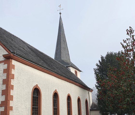 Kirche mit rotem Rand und Kreuz an der Fassade, daneben ein Baum mit roten Beeren., &copy; TI Bitburger Land - Steffi Wagner