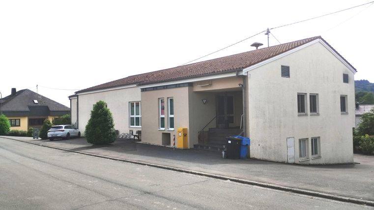 A simple building on a street with several windows. In front of the building, there is a car and a trash container.
