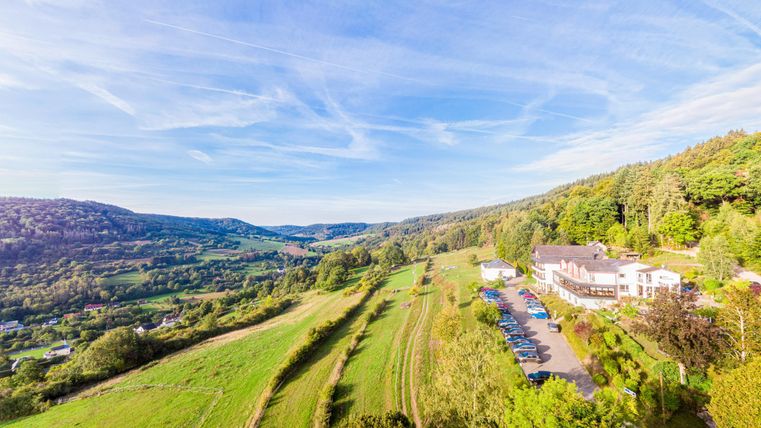 Le paysage pittoresque avec des collines douces et un vert luxuriant. Au premier plan se trouve l'hôtel forestier Sonnenberg, entouré d'arbres et d'un parking.
