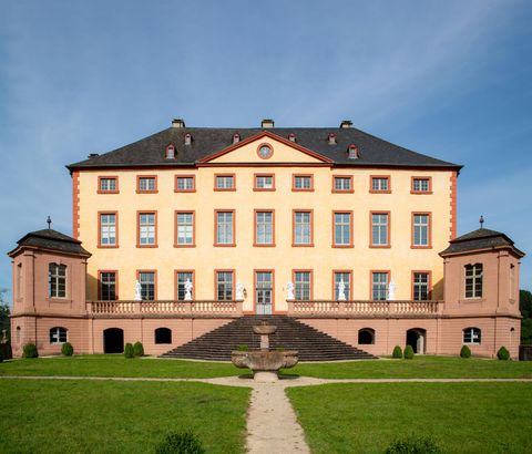 Ein historisches Schloss mit einer eleganten Fassade und großen Fenstern. Es liegt in einer grünen Umgebung mit einem gepflegten Garten.