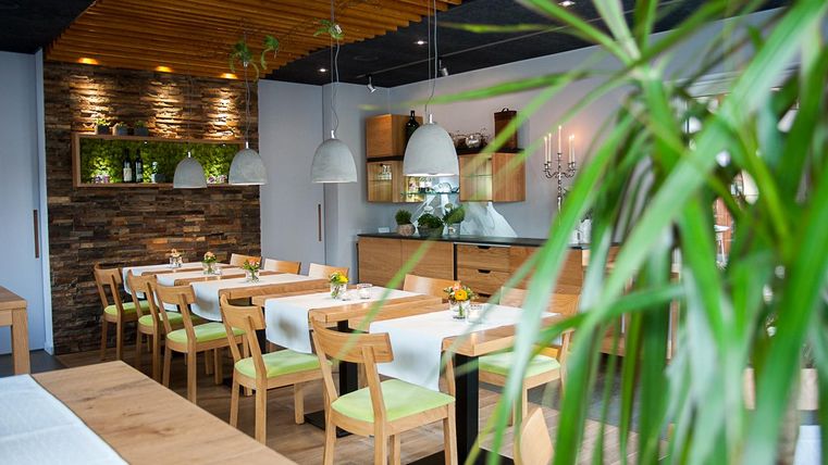 Een modern restaurant met lichte tafels en stoelen. De muren zijn versierd met hout en planten, en er zijn stijlvolle lampen.