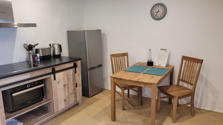 A modern kitchen with a dining table and two chairs. In the background, a refrigerator and various kitchen appliances are visible.
