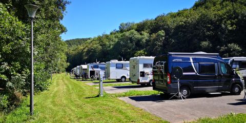 A campsite with several motorhomes amidst trees. The meadow is green and well-maintained.