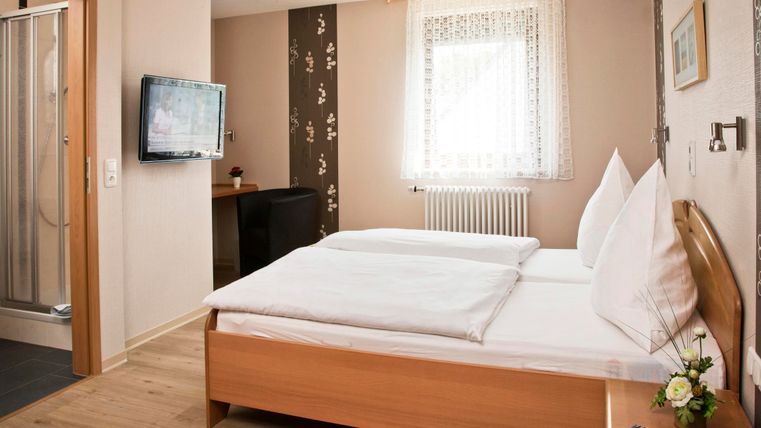 A bright room with two beds and a television. The bathroom is separated by a glass wall and there is a nice window front.