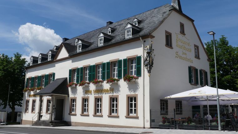 A traditional building with green shutters and flowers on the ground floor. There is an outdoor area with tables and chairs.