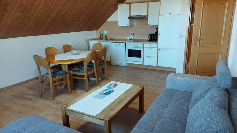 A bright, cozy apartment with an open kitchen and a dining area. The living room is furnished with a gray couch and a wooden table.