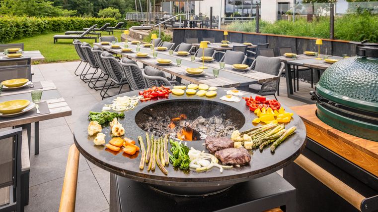 A modern outdoor grilling station, surrounded by a well-maintained garden. On the table, a variety of vegetables and meats are prepared for grilling.