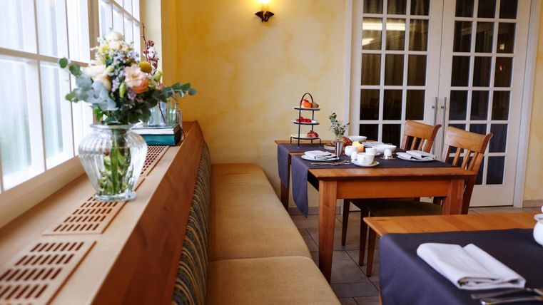 An inviting restaurant with wooden chairs and tables. The table is decorated with flowers and a tea stand.