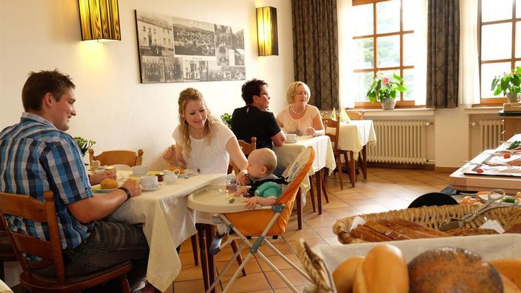 A cozy restaurant with a family at the table. On the table, various breakfast dishes and fresh rolls can be seen.
