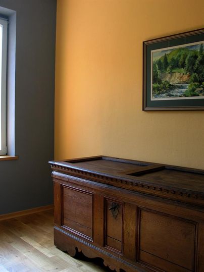 A cozy room with a large wooden chest and a painting on the wall. The walls are painted in soft colors, and the light falls through the window.