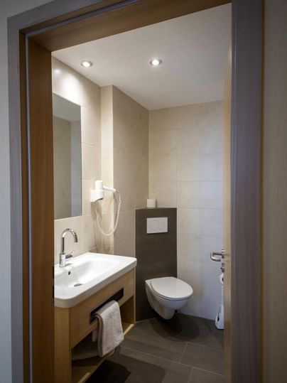 A modern bathroom with a sink, a toilet, and a large mirror. The walls are brightly tiled and the lighting is pleasant.