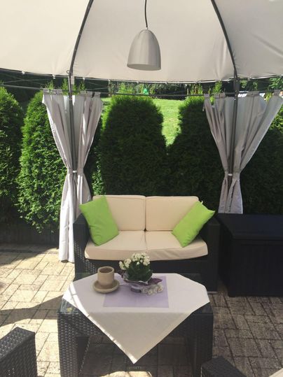 A cozy garden area with a sofa and cushions in green. A table with a plant and a coffee cup creates an inviting atmosphere.