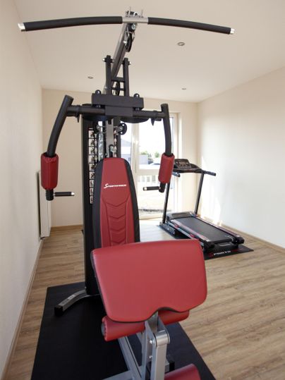 A modern gym with a weight station and a treadmill. The floor is covered with wood and the room is well lit.