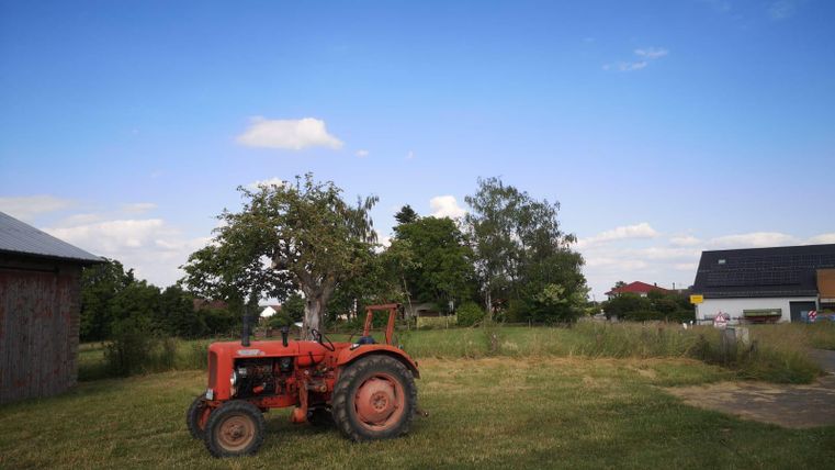 Un tracteur rouge est garé sur une pelouse avec quelques arbres en arrière-plan. Le ciel est bleu avec quelques nuages.