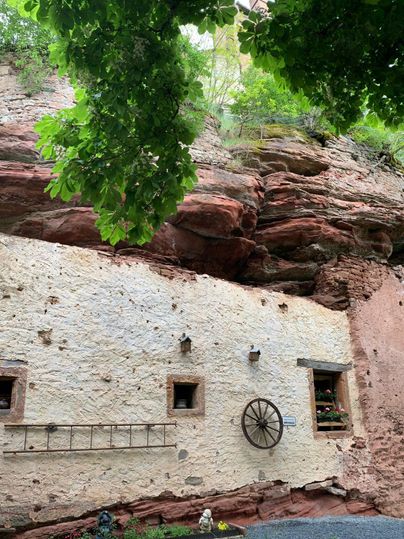 An old, charming stone wall, surrounded by red rocks and lush greenery. In the foreground, windows and a decorative wagon wheel decoration are visible.