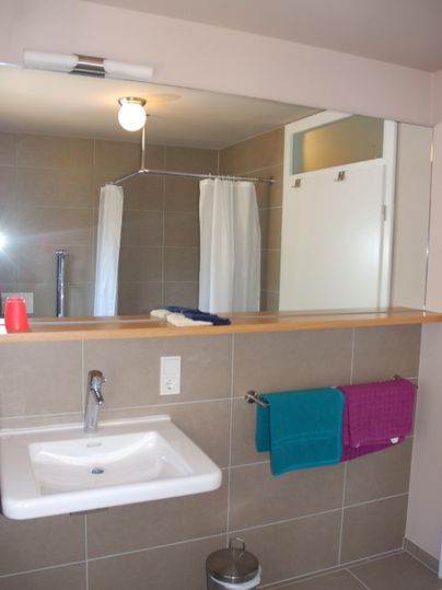A modern bathroom with a sink and a mirror. Towels in various colors hang next to the sink.