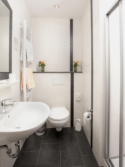 A modern bathroom with a shower, sink, and toilet. Fresh flowers and towels create an inviting atmosphere.
