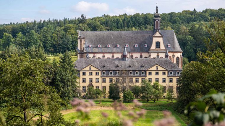 Kloster Himmerod inmitten grüner Landschaft mit bewaldetem Hintergrund.
