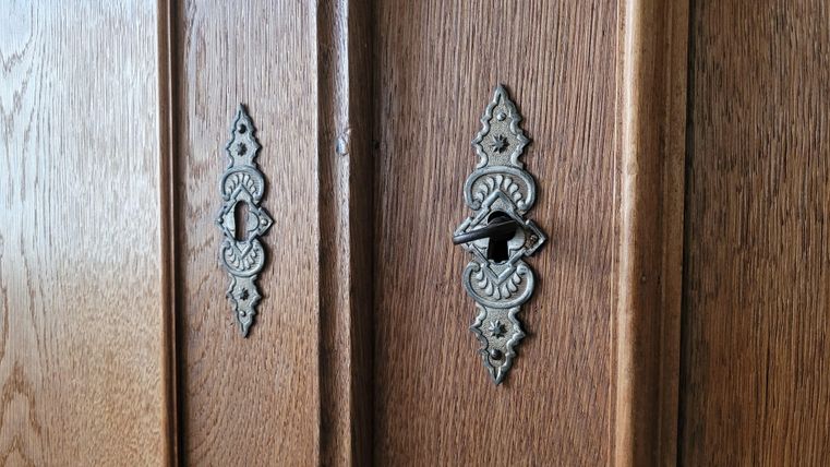 Close-up of two antique wooden cabinets with decorative locks. The surfaces are made of fine wood with a delicate grain.