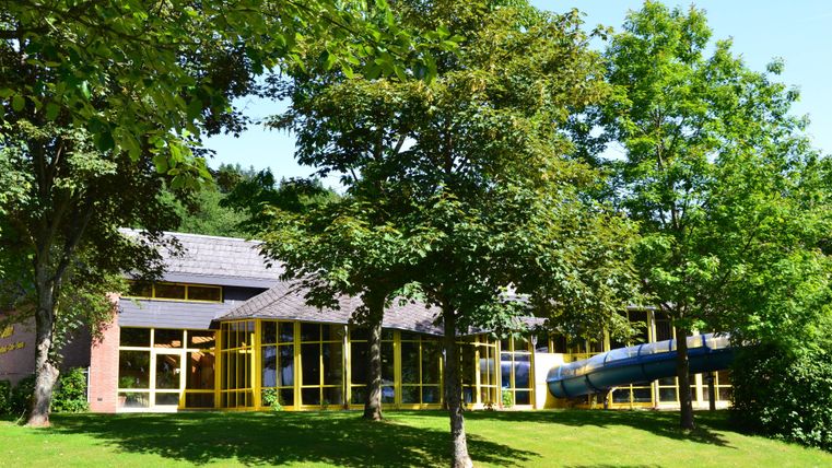 A modern building surrounded by trees and grass. A slide can also be seen near the entrance.
