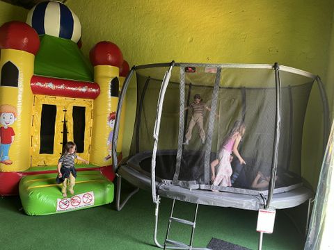 Ein Spielbereich mit einem hüpfenden Schloss und einem Trampolin. Kinder spielen und springen fröhlich in der bunten Umgebung.