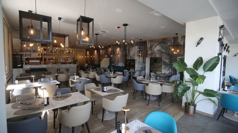 Een modern restaurant met elegante tafels en comfortabele stoelen. De warme lichten en planten creëren een uitnodigende sfeer.