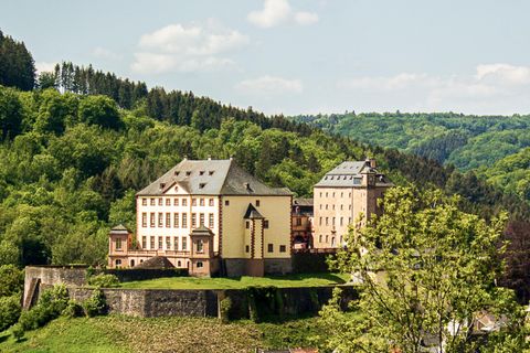 An impressive castle on a hill, surrounded by green forests. The architecture is historic and well-preserved.