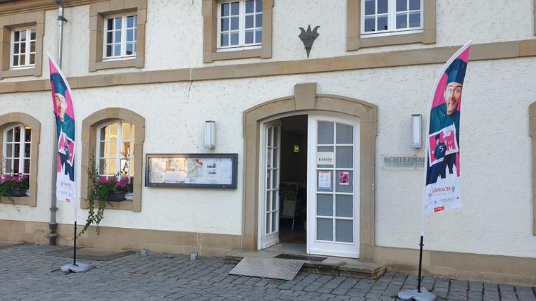A historic building with an inviting entrance.
In front of the building, there are two flags and flower boxes with plants.