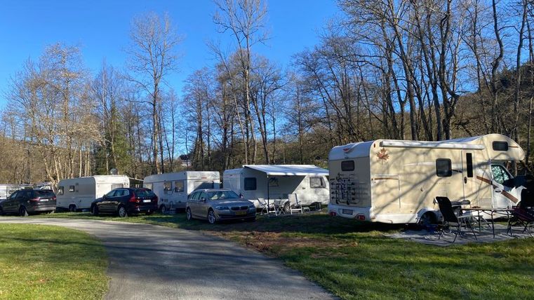 Un parc de camping-cars entouré d'arbres. Plusieurs camping-cars et voitures sont stationnés le long d'un chemin sinueux.