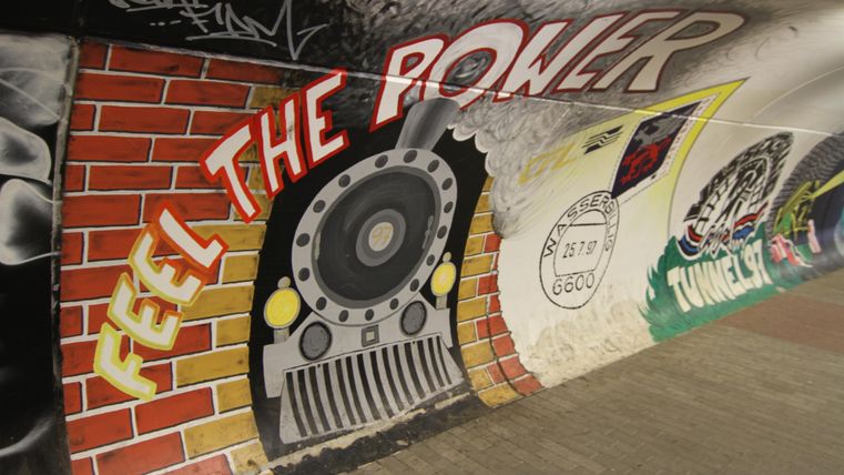 Een grafisch muurschildering met een stoomlocomotief-thema en de tekst "FEEL THE POWER". De kleuren zijn levendig en het ontwerp straalt een dynamische sfeer uit.