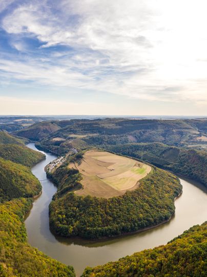 Luftaufnahme einer Flusslandschaft mit bewaldeten Hügeln und Feldern.