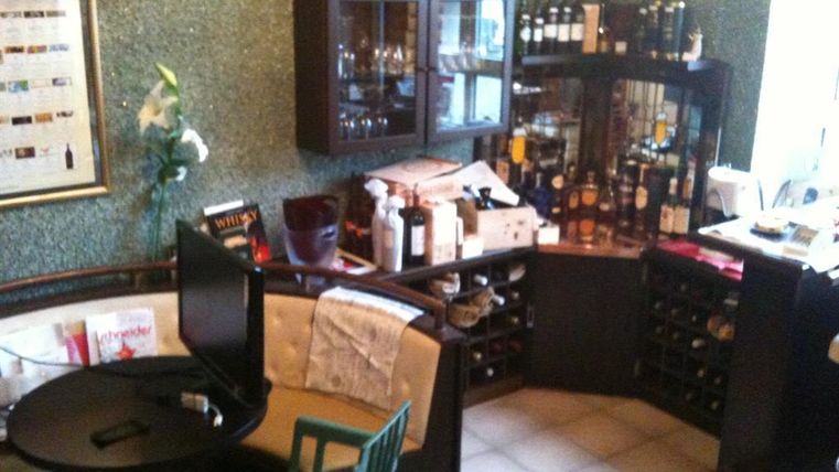 Een gezellige ruimte met een kleine tafel en stoelen. Aan de muur staan planken met wijnflessen en andere drankjes.