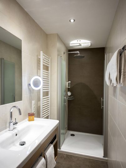 A modern bathroom with a shower and a sink. There are bright tiles and pleasant lighting.