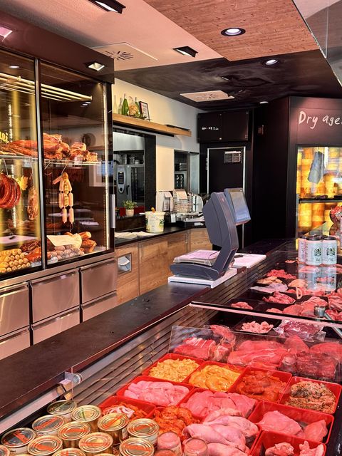 A well-organized butcher shop with fresh meat and various sausage products. In the background, a display case and work surfaces can be seen.