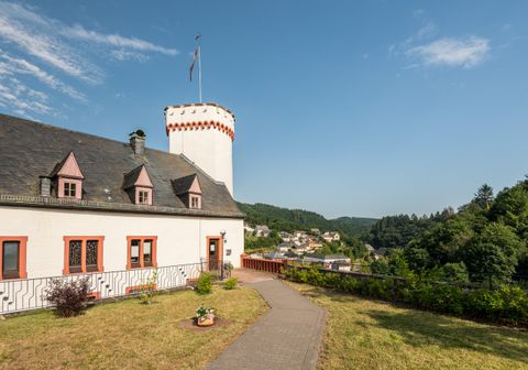 Een historisch gebouw met een toren en een mooie tuin. Op de achtergrond zijn groene heuvels en een klein dorp te zien.
