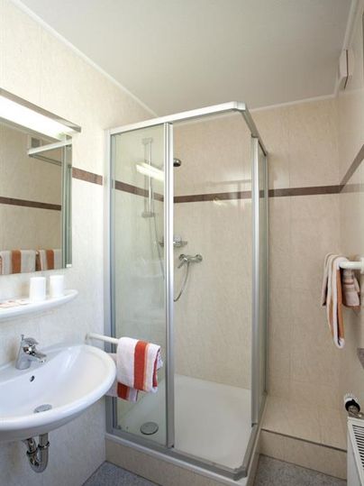 A modern bathroom with a shower cabin and a sink. The walls are light and simple, decorated with towels and personal care products.