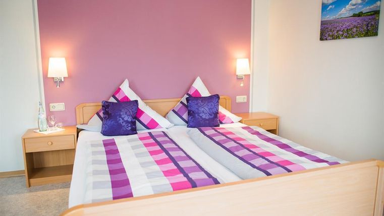A cozy bedroom with a large bed and colorful pillows. The walls are painted in a soft purple, and there are bright nightlights.