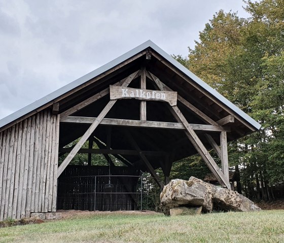 Un b&acirc;timent en bois avec un panneau 'four &agrave; chaux' se dresse dans un paysage forestier verdoyant. Le ciel est nuageux., &copy; TI Bitburger Land S.Wagner
