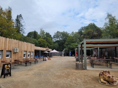 A cozy outdoor area with wooden huts and seating. In the background, trees and a tent can be seen.