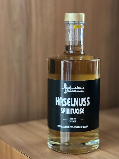 Een fles hazelnoot-likeur staat op een houten tafel. De fles heeft een eenvoudig etiket met de tekst "Hazelnoot Likeur".