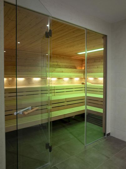 A modern sauna with glass sliding doors and warm wood interior. Soft lighting creates a relaxing atmosphere.