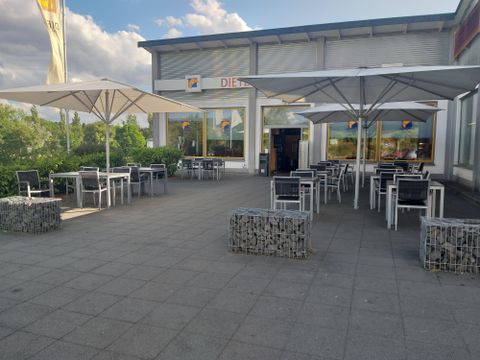 A modern outdoor terrace with tables and sun umbrellas. In the background, there is a shop with large windows.
