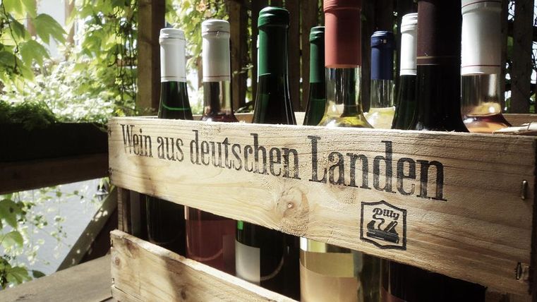 Een houten kist met verschillende wijnen uit Duitse streken. Op de achtergrond zijn groene planten te zien.